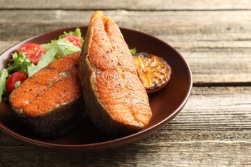Seafood. Tasty salmon steaks served with salad and lemon on wooden table, closeup. Space for text