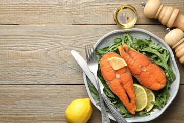 Seafood. Tasty salmon steaks served with arugula and lemon on wooden table, flat lay. Space for text