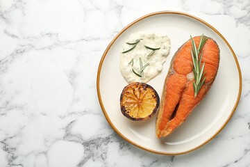 Seafood. Tasty salmon steak served with sauce, rosemary and lemon on white marble table, top view. Space for text