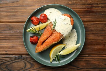 Seafood. Tasty salmon steak served with sauce, tomatoes, rosemary and lemon on wooden table, top view