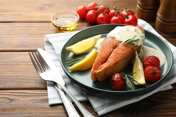 Seafood. Tasty salmon steak served with sauce, tomatoes, rosemary and lemon on wooden table, closeup