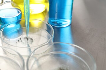 Dripping liquid from pipette into Petri dish at metal table, closeup