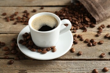 Aromatic coffee in cup and beans on wooden table, closeup