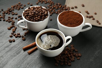 Cup of drink, ground coffee, beans and cinnamon on black table, above view