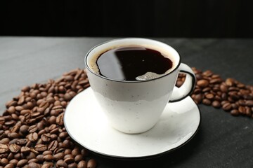 Aromatic coffee in cup and beans on black table, closeup