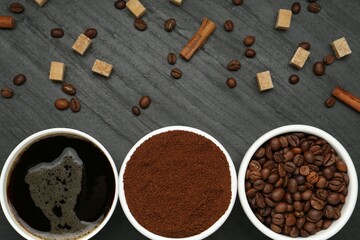 Cup of drink, ground coffee, beans, brown sugar and cinnamon on black table, flat lay