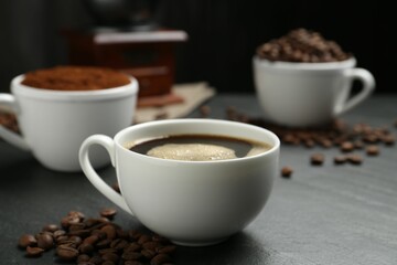 Cup of drink, ground coffee and beans on black table, closeup