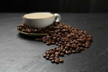 Aromatic coffee in cup and beans on black table, closeup