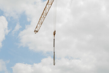 Obraz premium A tall crane on a construction site, blue sky. Construction crane in the sky. Yellow crane tower lifting up