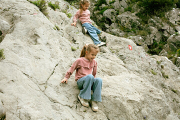two little girls sisters twins climbing on rock together outside