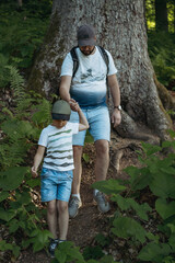 man and child trekking in forest descending from slope. Father supporting son holding him by hand
