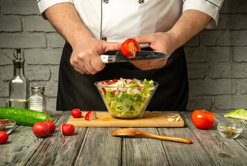 A chef is slicing tomatoes while preparing a fresh salad in a contemporary kitchen. Colorful vegetables like cucumbers and radishes surround the chef, creating a vibrant atmosphere