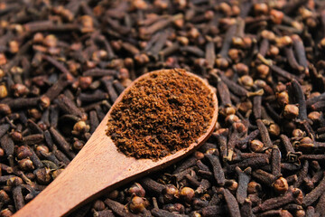Clove powder on a wooden spoon with cloves background. Aromatic ingredients