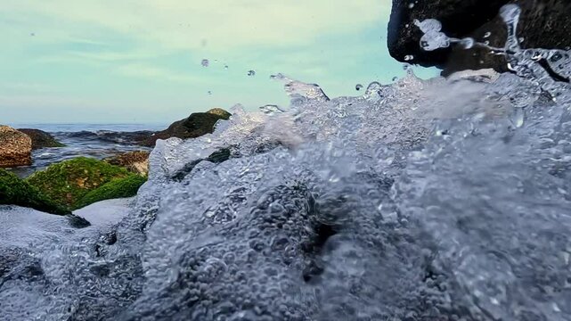 Fast flow of fresh water with foam and air bubbles in the Black Sea, washing stones with green and red algae