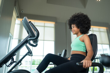 African American girl with curly hair working out on exercise bike in gym sports club