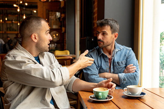 Two men are having a serious disagreement while drinking coffee in a cafe, showing tension and conflict