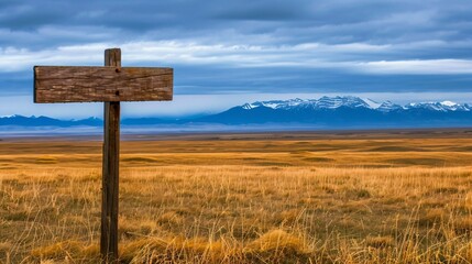 Golden prairie landscape with wooden trail sign pointing towards mountains under dramatic sunset. Concept of adventure, exploration and untouched natural beauty in wilderness.