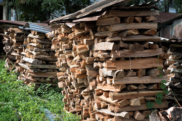 Stacked Firewood Under Metal Roofing in Rural Yard - Neatly arranged stacks of split firewood are sheltered under corrugated metal sheets in a grassy rural area. 