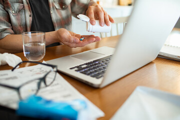 Close up man taking medicine while working from home with laptop