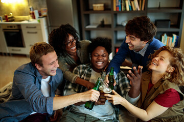 Diverse group of friends laughing and toasting with beer bottles at home party gathering