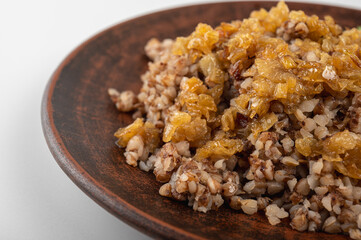Traditional buckwheat porridge with caramelized onions on a rustic plate. A hearty, nutritious and aromatic dish, popular in Eastern European cuisine, on a clay plate, on a white background