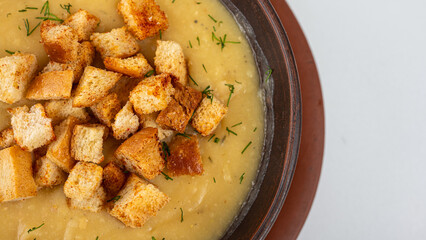 Creamy pea soup with golden croutons and fresh dill served in a clay bowl. Traditional homemade comfort food, top view, rustic style