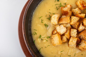 Creamy pea soup with golden croutons and fresh dill served in a clay bowl. Traditional homemade comfort food, top view, rustic style