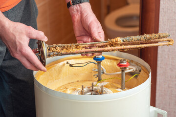 A worker holds a heating element of an electric boiler covered in rust and mineral deposits. Boiler maintenance and repair