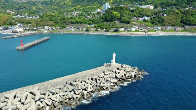 Aerial View of Long Tetrapod Breakwater with Waves Crashing - Scenic Coastal Town in Background
