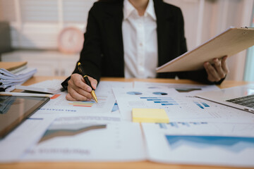 An Asian businesswoman analyzes financial data on her laptop during a corporate meeting, collaborating with colleagues on strategy, reports, and teamwork.