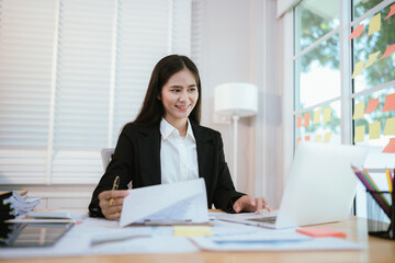 An Asian businesswoman analyzes financial data on her laptop during a corporate meeting, collaborating with colleagues on strategy, reports, and teamwork.