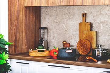 Kitchen countertop with utensils, pans on induction hob, bowls, cutting boards, vegetables