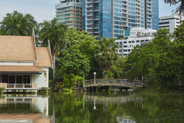 Modern skyscrapers reflect in peaceful lake beside traditional architecture in urban park setting