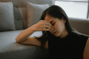 A distressed young adult woman sits alone indoors, experiencing sadness, anxiety, and emotional...