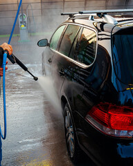 A sleek black car getting a thorough wash with pressurized water and cleaning agents.