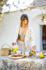 A woman prepares a Mediterranean meal on a rustic stone table in front of a trullo in Puglia. The image captures natural living and slow food concepts for lifestyle and culinary branding