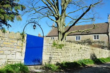 Wooden gated entrance with a lantern and stone wall of a beautiful cottage house on a village street in the English countryside