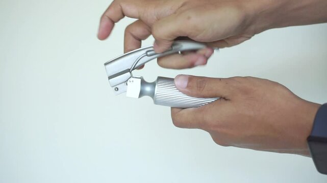 A hand holding a laryngoscope against a white backdrop. Laryngoscope, a simple drawing of a medical instrument for examining the larynx, an otolaryngologist&rsquo;s inventory.