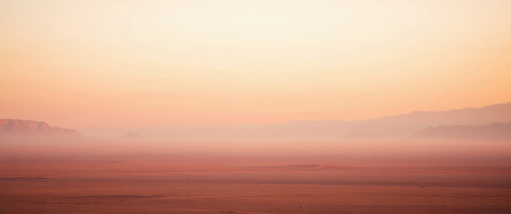 Fototapeta premium Pink sunrise illuminating foggy desert landscape with mountains