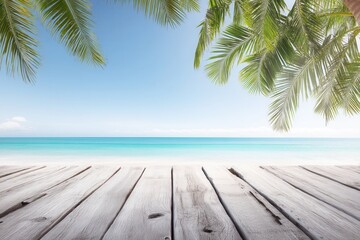 Sunlit wooden deck with palm trees overlooking a sandy beach and clear blue sky at daytime.