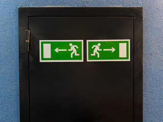 Two emergency exit signs with running figure and arrows pointing left and right placed on black...