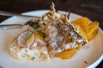 A close-up of crispy fried fish skin and potato chips, served with creamy salad and pickled red onions on plate