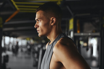 Obraz premium Side view close up portrait of serious concentrated man, breathing while taking a break from workout, training or exercising inside a fitness gym. Bodybuilding, fitness and health care concept