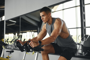 Side view of Caucasian athletic male cardio riding on bicycle at gym fitness. Muscular people...