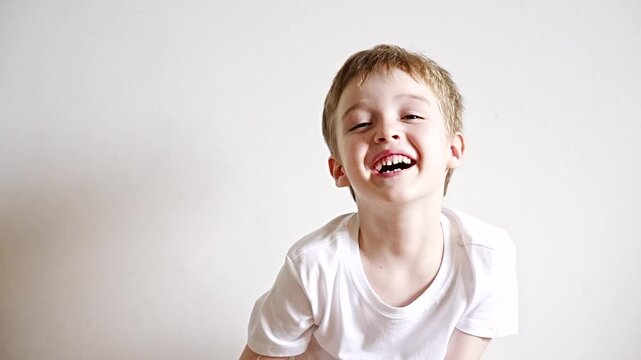 boy 5 years old with blond hair and blue eyes in a white t-shirt on a white background laughs and smiles at the camera