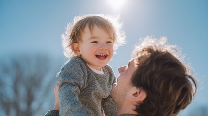 A joyful child is held high by a smiling parent under a bright blue sky, radiating happiness and warmth.