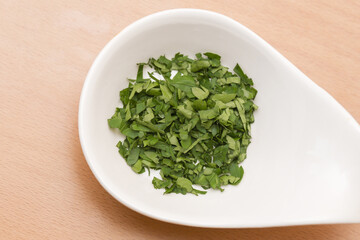 Fresh chopped cilantro in white ceramic spoon on wooden table. Herb ready for cooking. Simple kitchen scene. Natural food background. Healthy ingredient closeup. Culinary concept for cooking.