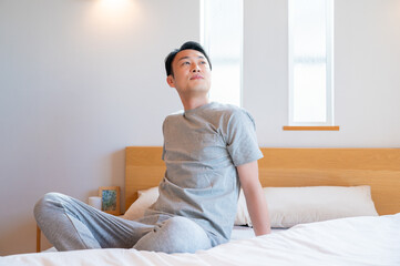 ベッドの上で座りながら遠くを見つめる男性の静かな朝のひととき