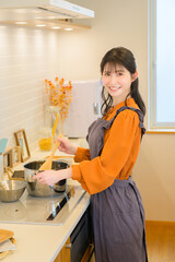 エプロン姿の女性がキッチンで鍋をかき混ぜながら微笑む料理シーン