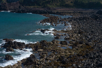 Rocky shoreline landscape, natural style, blue and earthy tones, Jeju South Korea Umutgae Coast Seongsan Ilchulbong, dramatic waves and volcanic rocks